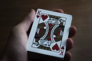 A hand playing cards with the King of Hearts.